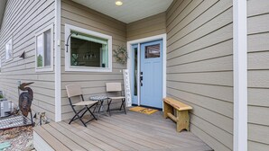 Ein Haus mit Veranda, einer blauen Tür, einem Willkommensschild, einer Bank und Gartenmöbeln.