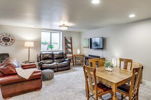 A living room with a leather sofa, a wooden dining table, and a television mounted on the wall. - Next to Public Golf Course! Kalispell Townhome (Kalispell)