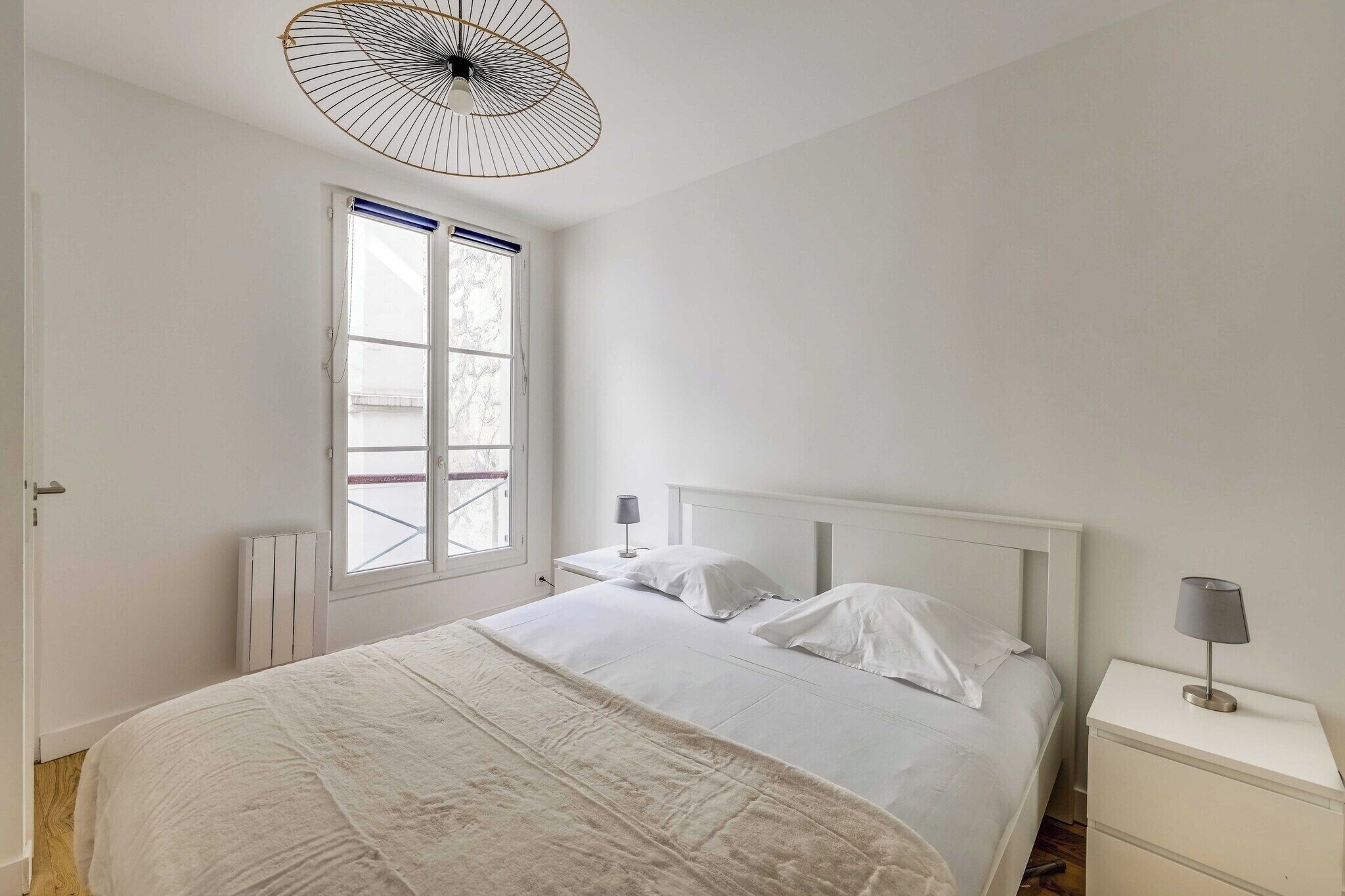 Een slaapkamer met een bed, nachtkastjes, een raam en een plafondventilator.