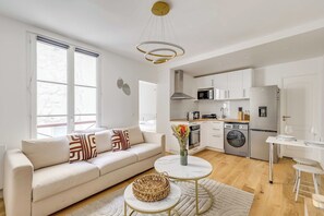 A modern living room with a sofa, a coffee table, and a kitchen area with appliances. - Modern Apartment 1BR/4P - Paris 10th (Paris)