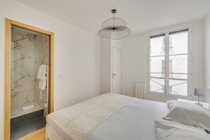 Ein Schlafzimmer mit Bett, einem Fenster mit Jalousien, einer Tür und einem Duschbereich.