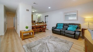 Een woonkamer met een bank, een vloerkleed en een eethoek met een tafel en stoelen.