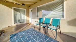 Een overdekt terras met een blauw gestreept tapijt, drie stoelen en een raam met zonwering.