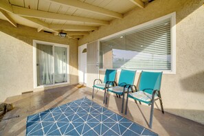 Un patio cubierto con un tapete azul estampado, tres sillas y una ventana con persianas.