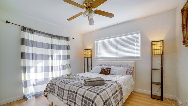 Een slaapkamer met een bed, een plafondventilator, een raam met jaloezieën en bedlampen.