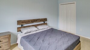 Une chambre à coucher avec une tête de lit en bois, un lit recouvert d’une couette grise, une table de chevet et une porte blanche.