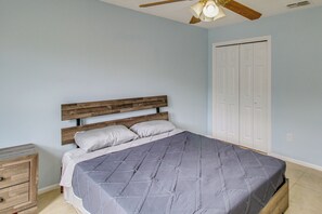 A bedroom with a wooden headboard, a bed with a grey quilt, a nightstand, and a white door. - Private Patio! Family Home in Corpus Christi (Corpus Christi)
