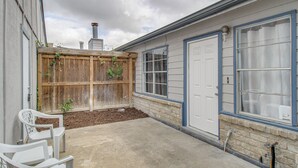 Un jardin à l’arrière d’une maison, avec une clôture en bois, une terrasse en béton et une porte de garage blanche.