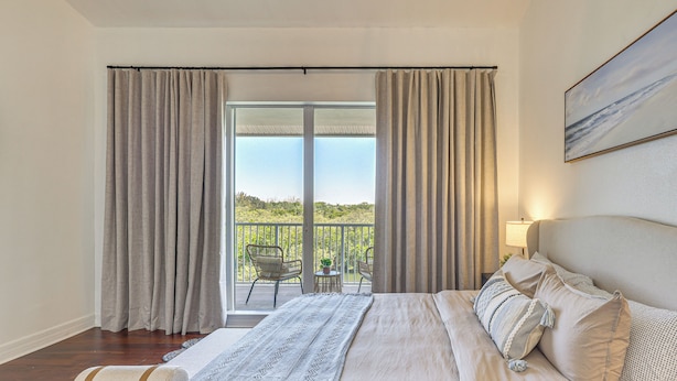 Quarto com cama grande, vista para o exterior e varanda com cadeiras.