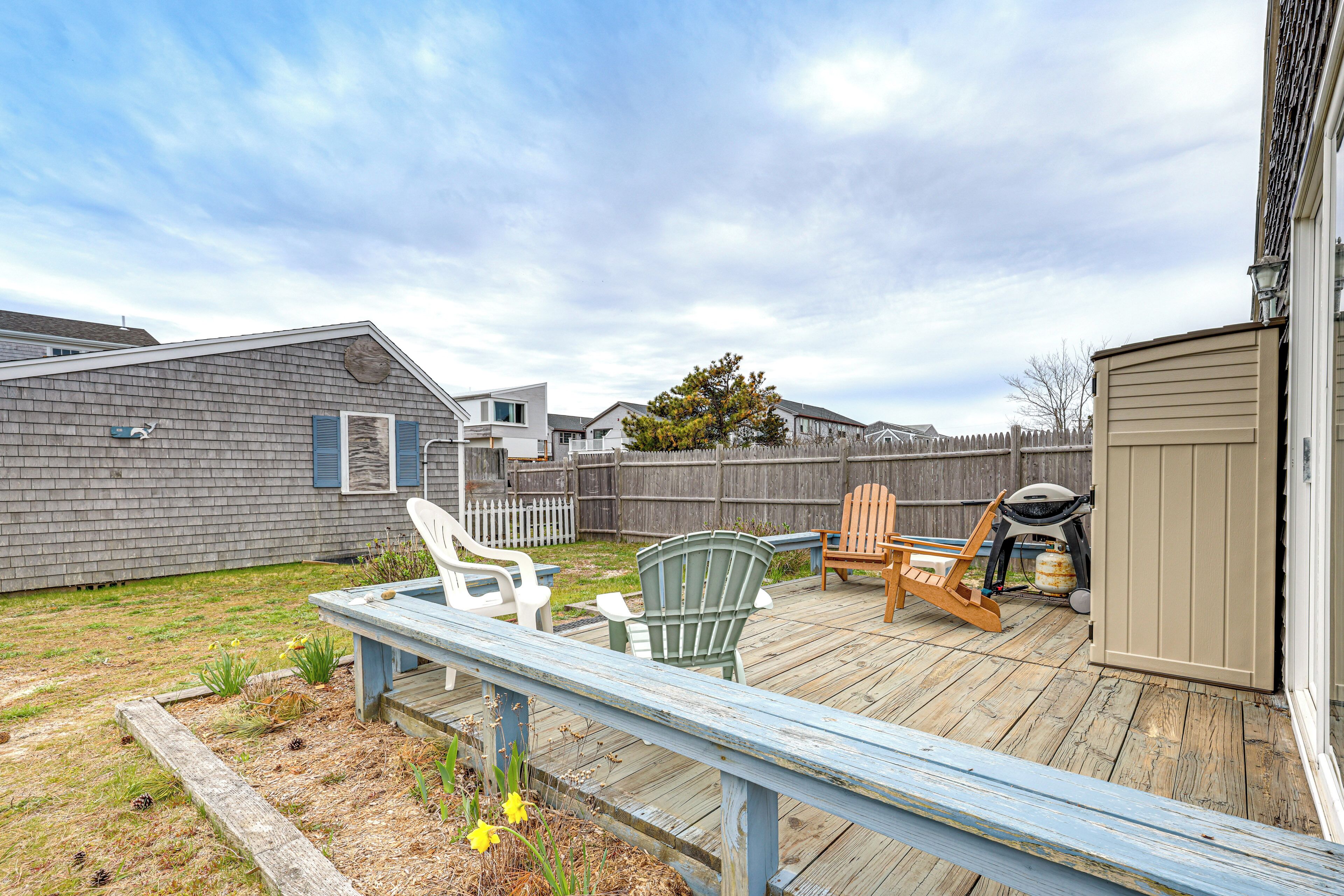A deck with chairs and a grill, surrounded by a wooden fence and a shed.