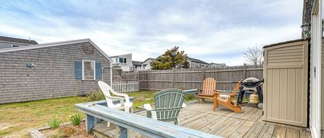 A deck with chairs and a grill, surrounded by a wooden fence and a shed.