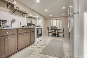 A kitchen with wooden cabinets, a stove, and a dining area with a table and chairs. - Walk to Theaters & Dining! Ridgefield Gem w/ Yard (Ridgefield)