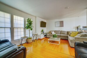 A spacious living room with a large window, a sofa set, a coffee table, and a TV mounted on the wall. - Family Gem w/ Pet-Friendly Yard! 8 Mi to Riverside (Moreno Valley)