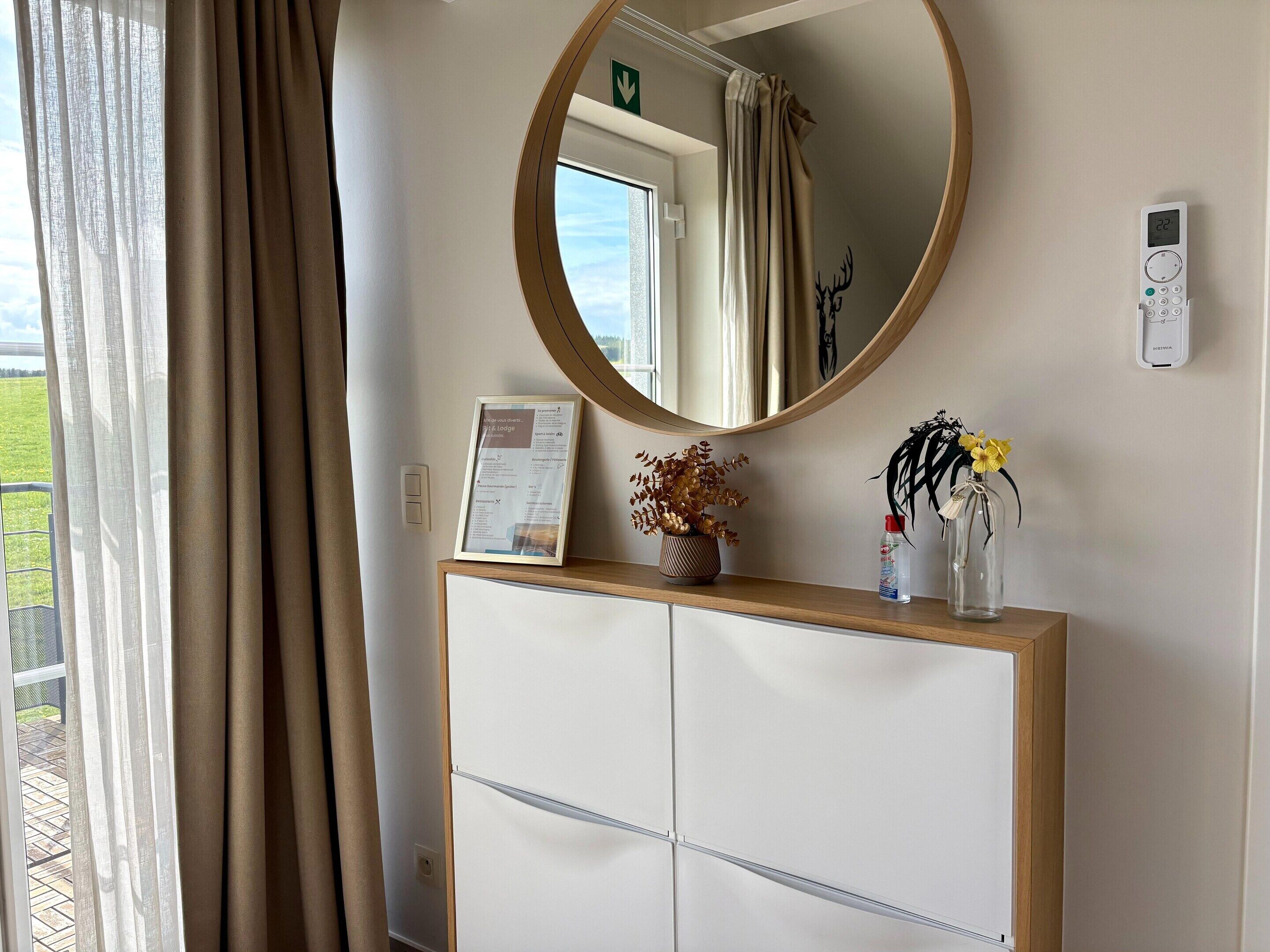 A room with a large mirror, a framed sign, a small vase with dried flowers, and a thermostat on the wall.