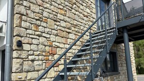 Un bâtiment en pierre avec un escalier métallique menant à une fenêtre.
