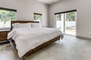A modern bedroom with a large bed, a wooden headboard, and a view of the outdoors through large windows. - Private Yard & Covered Patio: Modern Tampa Getaway (Tampa)