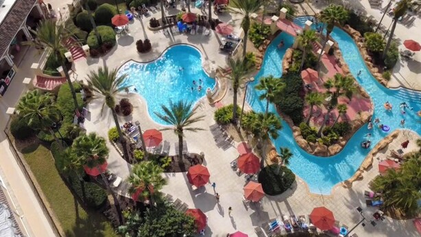 An aerial view of a resort with a large pool area, palm trees, and sun umbrellas. - Pet-Friendly Townhome 9 Mi to Disney w/ Lazy River (Davenport)