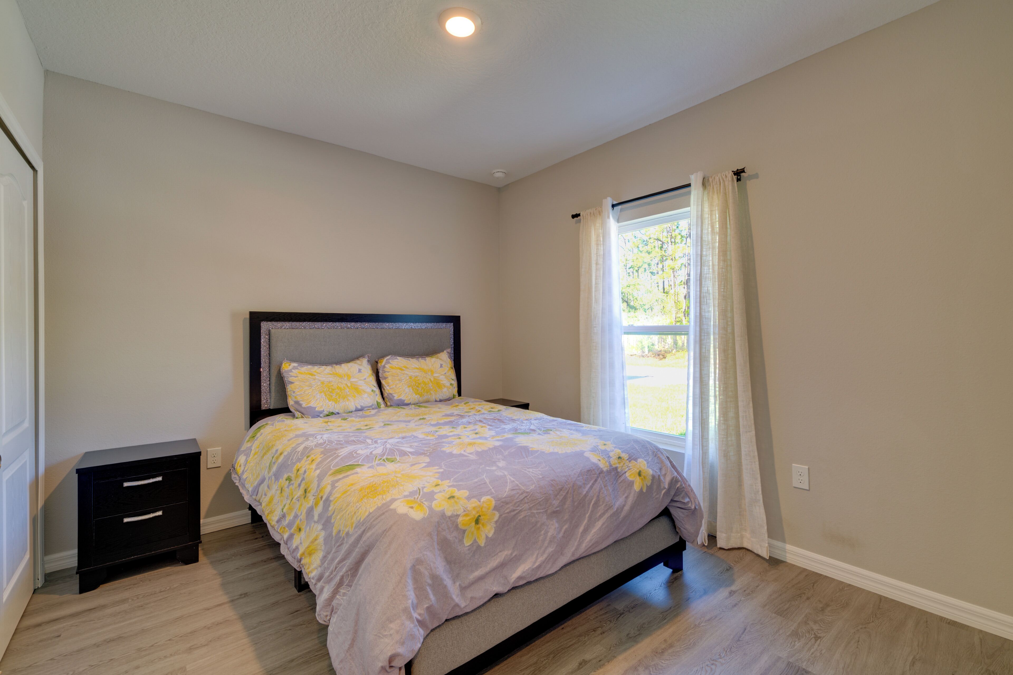Une chambre à coucher avec un lit, une table de chevet, une fenêtre avec des rideaux et un luminaire au plafond.