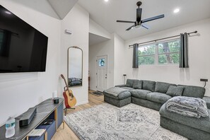 Una sala de estar moderna con un sofá modular, un televisor de pantalla plana, un ventilador de techo y un ventanal con cortinas.