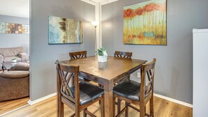 Een eetruimte met een houten tafel en stoelen, een vaas met bloemen en twee schilderijen aan de muur.