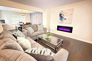 A living room with a sectional sofa, a glass coffee table, a fireplace, and a dining area in the background. - Refined Decatur Retreat: Shop, Dine + Unwind! (Decatur)