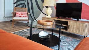 A living room with a sofa, a glass coffee table, a TV, a lamp, and a wall with abstract art. - Renovated duplex apartment in residence on 3rd floor with elevator. (Roscoff)