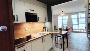 A modern kitchen with white cabinets, a wooden countertop, and a sink. There is a dining area with a table and chairs, and a large window providing natural light. - Renovated duplex apartment in residence on 3rd floor with elevator. (Roscoff)