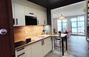 A modern kitchen with white cabinets, a wooden countertop, and a sink. There is a dining area with a table and chairs, and a large window providing natural light. - Renovated duplex apartment in residence on 3rd floor with elevator. (Roscoff)