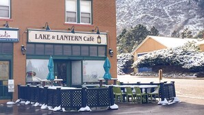 En café med udendørs siddepladser, murstensfacade og et bjerg i baggrunden.