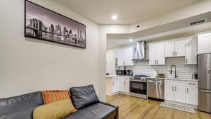 Une cuisine moderne avec des meubles blancs, des appareils en acier inoxydable et un tableau représentant un paysage urbain accroché au mur.