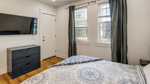 Une chambre à coucher avec un lit, une commode, une télévision et une fenêtre avec des rideaux.
