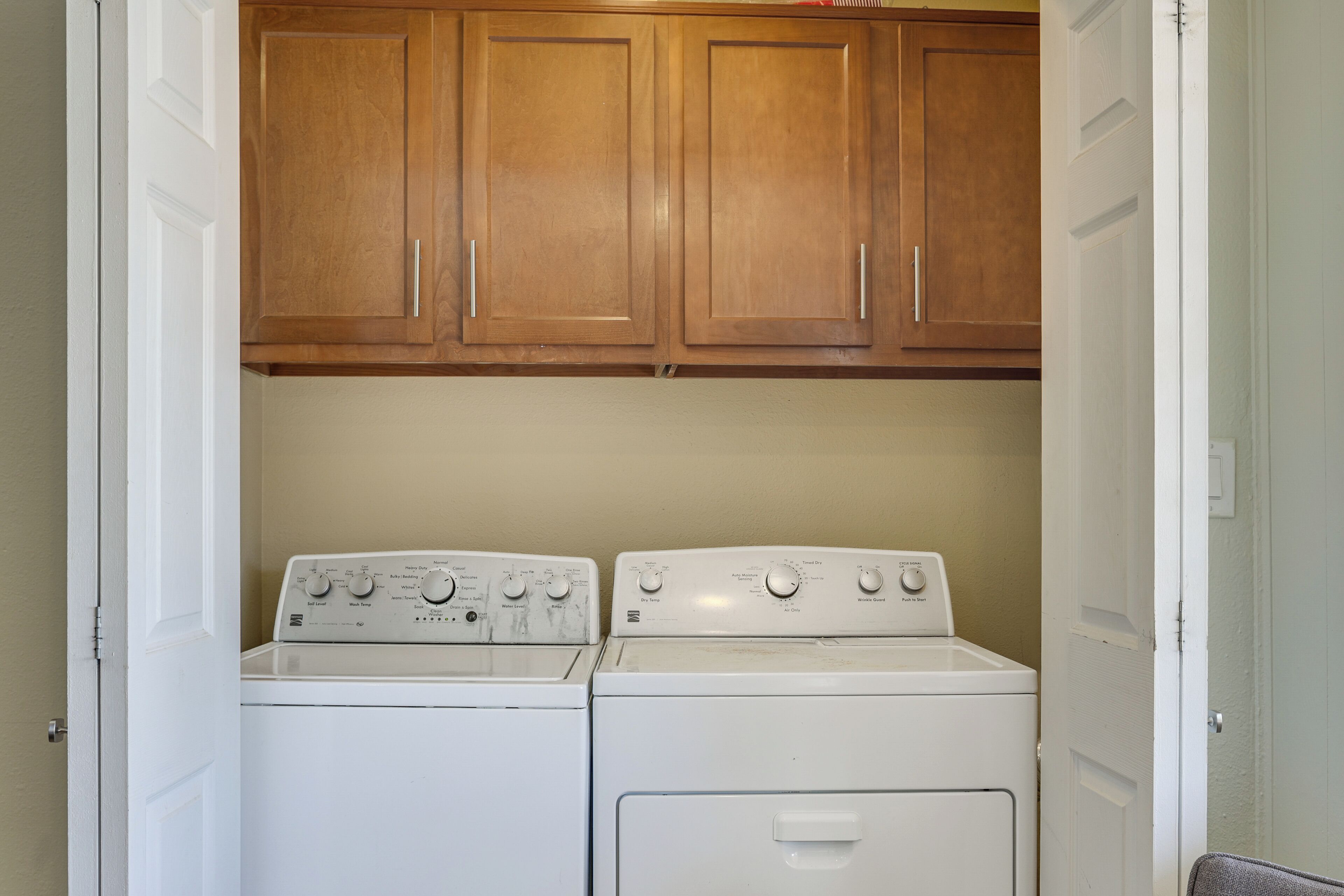 A laundry room with two white washing machines and wooden cabinets above.