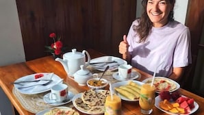 Una mesa de comedor con diversos artículos para el desayuno, incluyendo platos de comida, una tetera, tazas y un vaso de jugo.