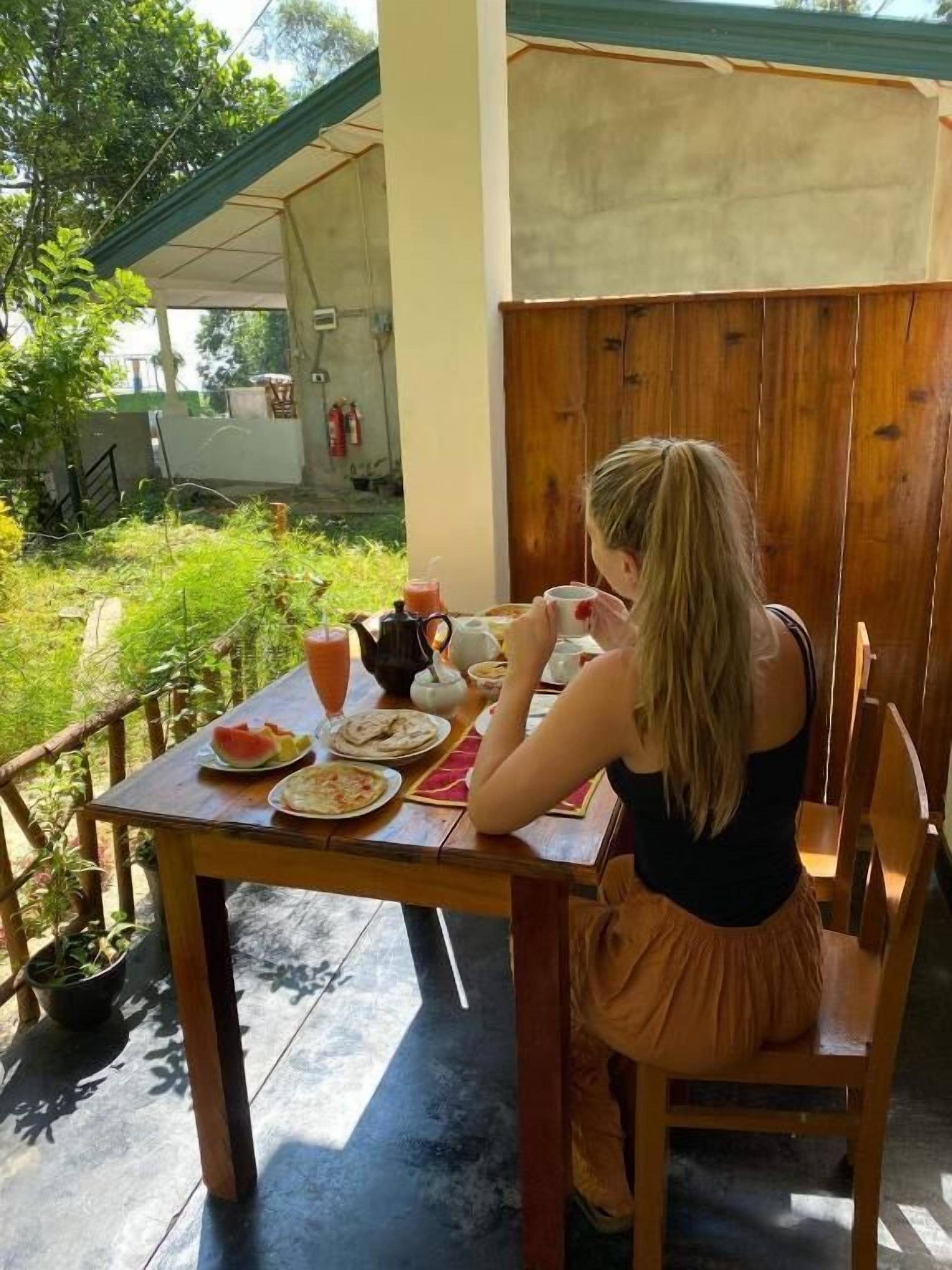 A person sitting at an outdoor table with a meal, surrounded by greenery.
