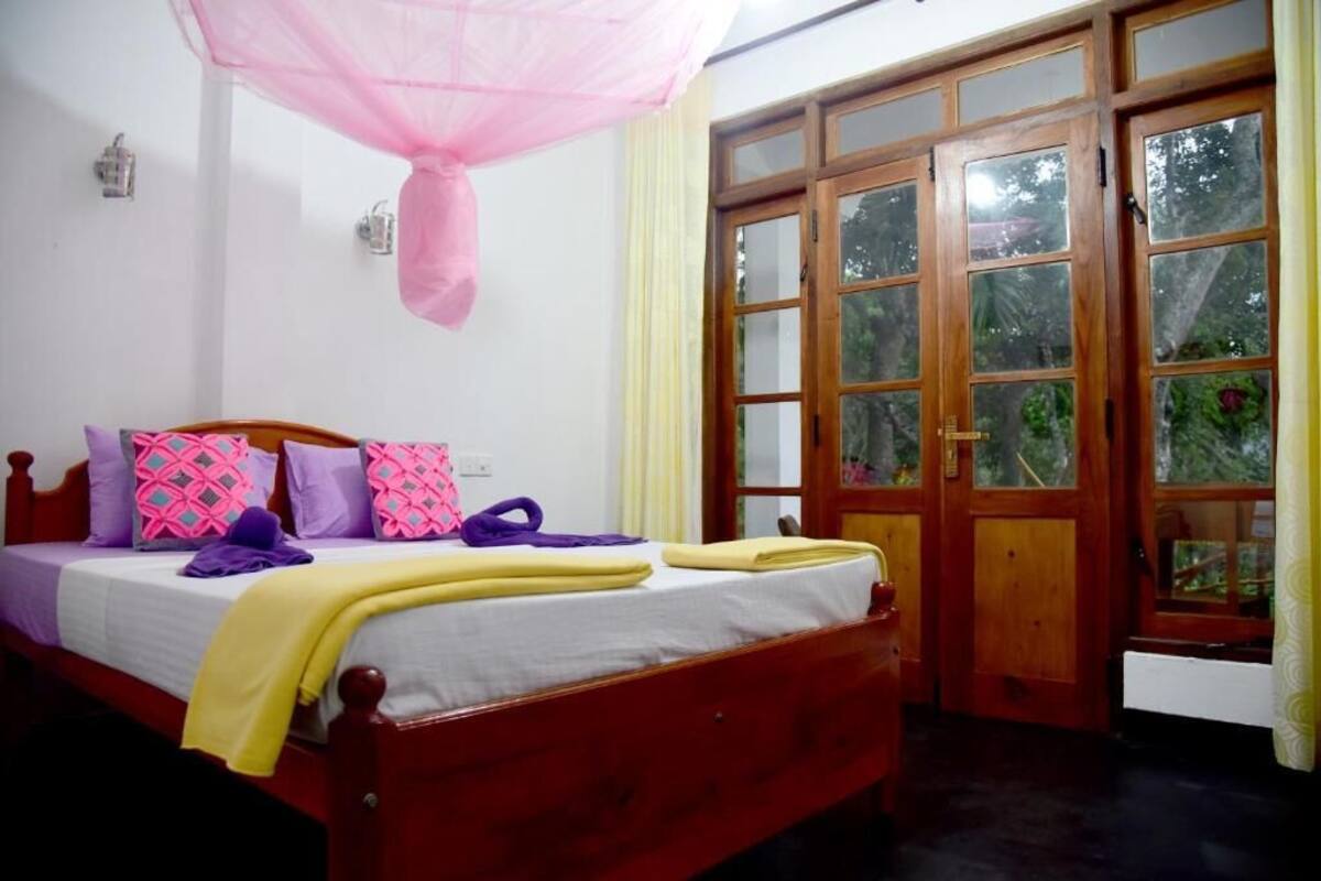 A room with a bed, a window with a view of greenery, and a door with glass panels.