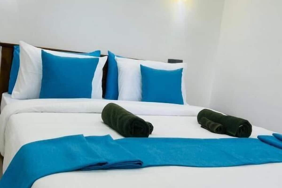 A neatly made bed with blue and white bedding, two rolled-up towels, and two wall-mounted lights.