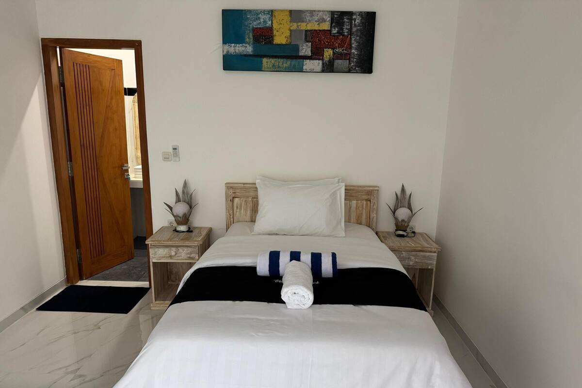 A bedroom with a bed, wooden headboard, bedside tables, a painting, and a door.