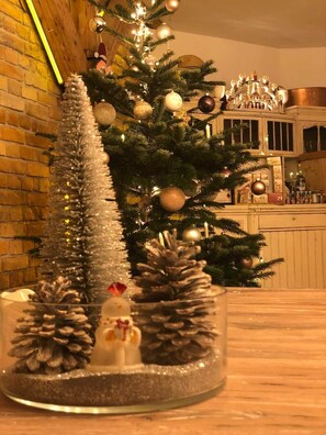 Ein Weihnachtsbaum mit Dekorationen und Tannenzapfen, eine Ziegelwand und ein Barbereich im Hintergrund.