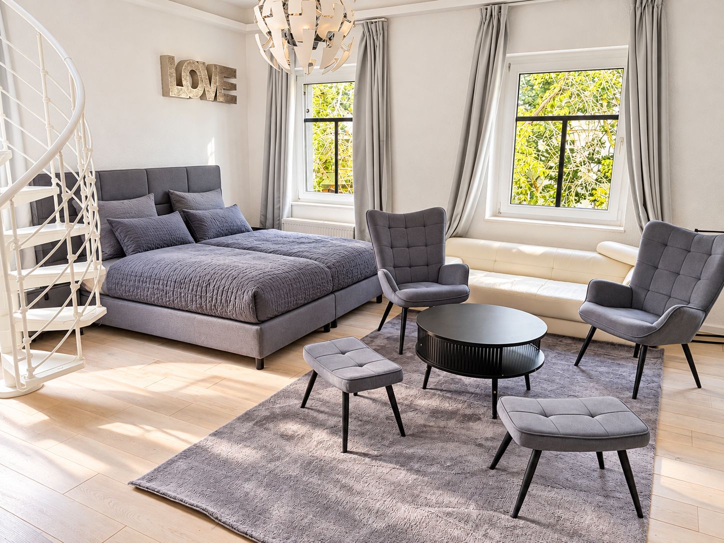 Ein modernes Schlafzimmer mit einem Bett, zwei Sesseln, einem runden Couchtisch und einer Couch.