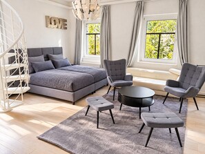 A modern bedroom with a bed, two armchairs, a round coffee table, and a sofa.