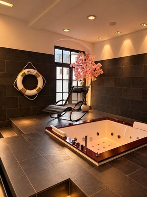 A spa room with a large bathtub, a massage chair, and a decorative flower arrangement.