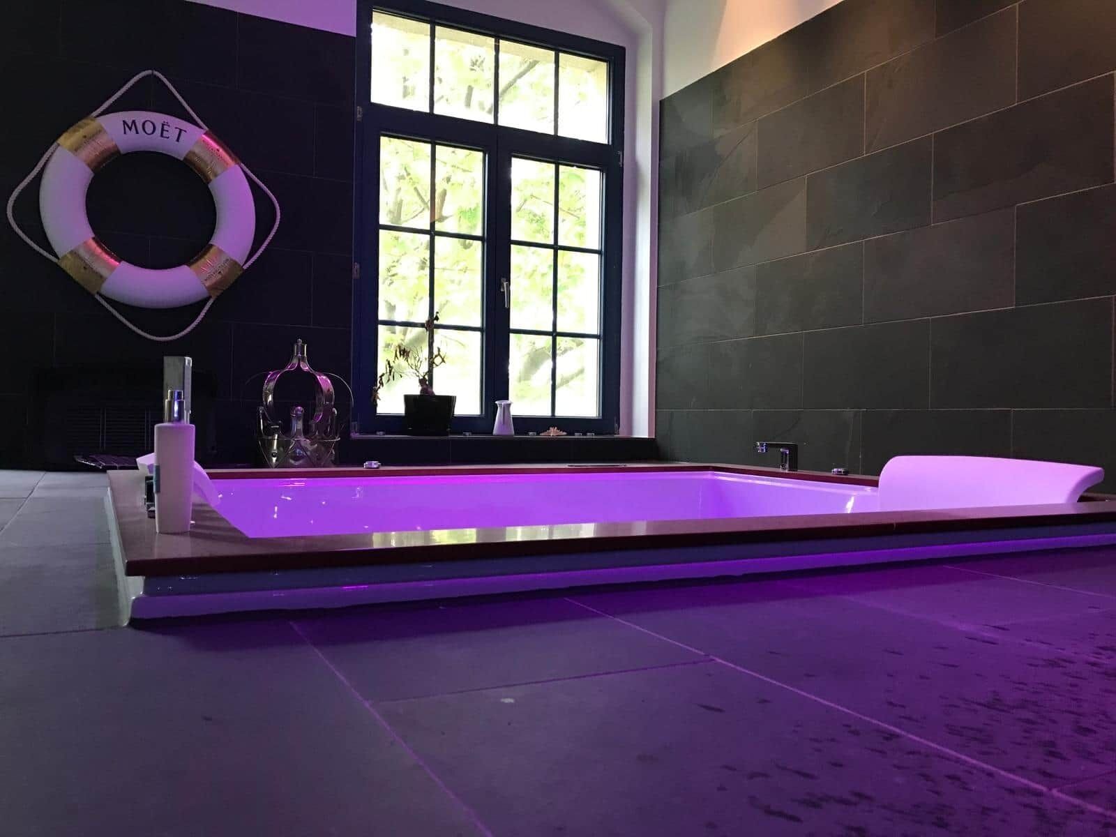 Une salle de bain moderne avec une grande baignoire, une fenêtre donnant sur un paysage verdoyant et un flotteur de sauvetage à l’effigie de la marque Moët accroché au mur.