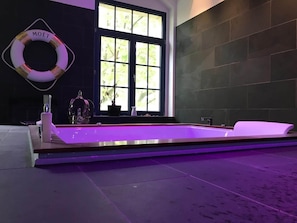 Ein modernes Badezimmer mit einer großen Badewanne, einem Fenster mit Blick auf Grünflächen und einem Moët Rettungsring an der Wand.