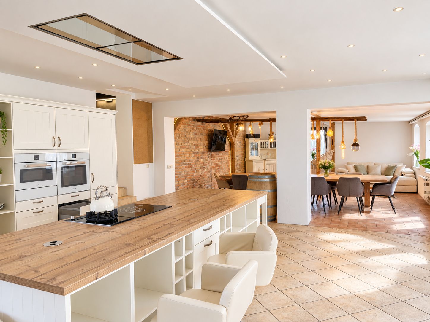 A modern kitchen with white cabinetry, a wooden countertop, and a dining area with a table and chairs.