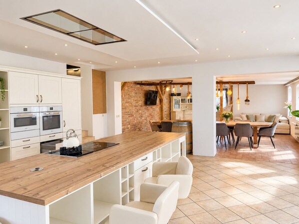 A modern kitchen with white cabinetry, a wooden countertop, and a dining area with a table and chairs.