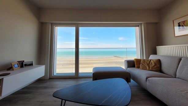 Un salon moderne avec un canapé, une table basse et une vue sur la plage grâce à de grandes portes coulissantes.