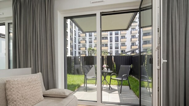 A modern living room with a sofa, a glass sliding door leading to an outdoor patio with a table and chairs.