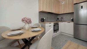 A modern kitchen with wooden cabinets, a stainless steel refrigerator, and a dining area with a round table set for two.