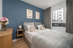 Ein Schlafzimmer mit einem Bett, einem Nachttisch, einem Fenster mit Vorhängen und zwei Wandbildern.