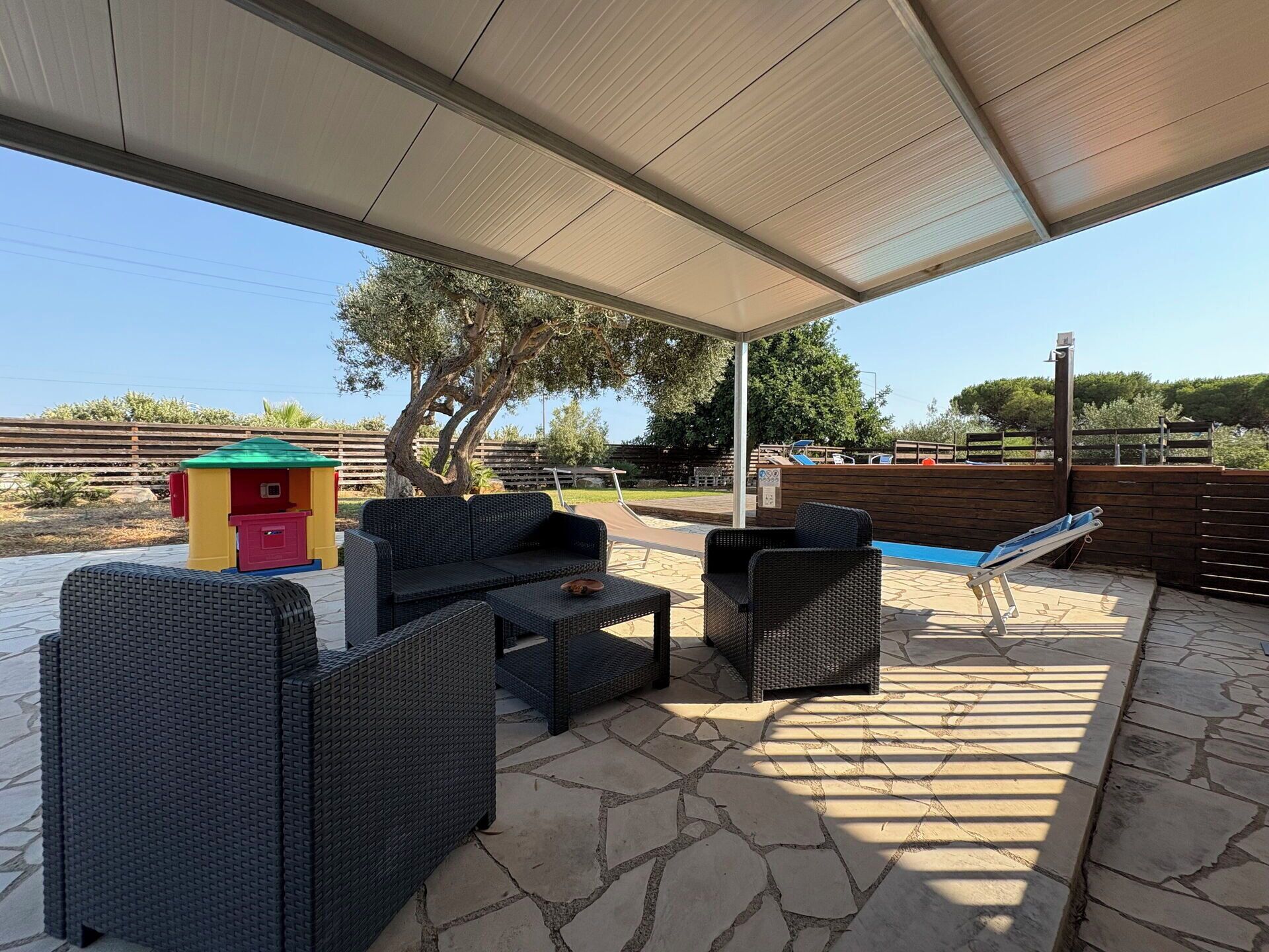 Un patio exterior con mobiliario de mimbre, una piscina y una zona techada.